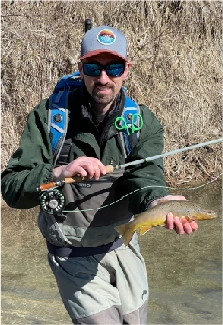 Angler standing in a small creek holding a brown trout and a fly rod